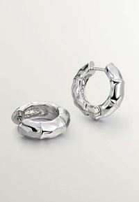 Pendientes de aro de bambú plateado con una superficie texturizada y forma circular, que presentan un acabado brillante y un herraje visible para el cierre.
