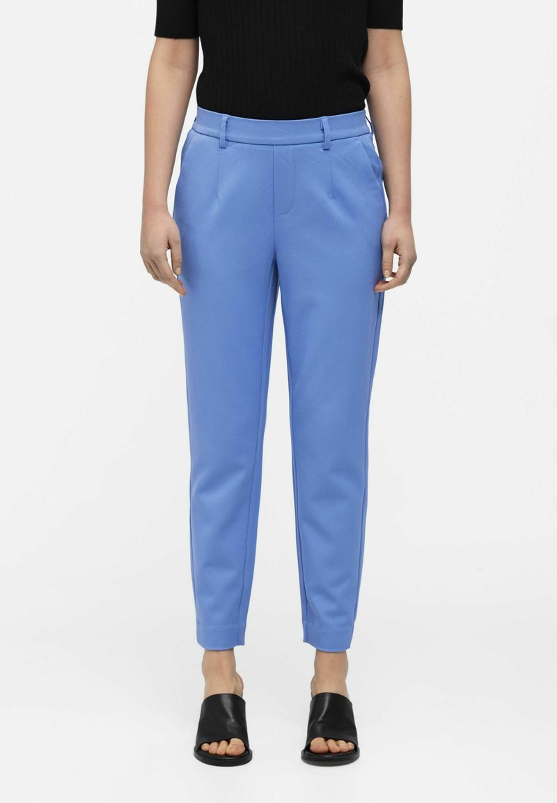 Pantalons ajustés bleu clair avec une texture lisse, une coupe fuselée et deux poches avant, associés à des sandales à semelle plate noires.