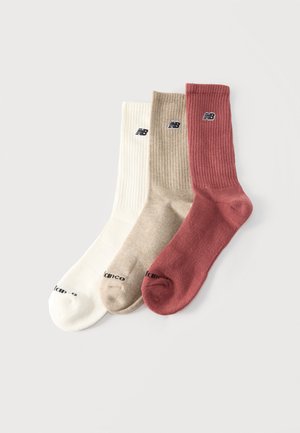 Drei New Balance gerippte Knöchelsocken in Weiß, Beige und Rost, nebeneinander auf einem einfarbigen Hintergrund ausgelegt.