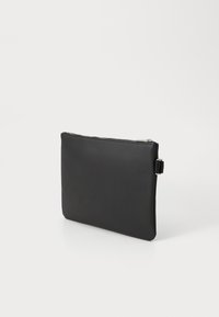 Pochette rectangulaire noire avec fermeture éclair, surface texturée et boucle latérale, se tenant debout sur un fond blanc.