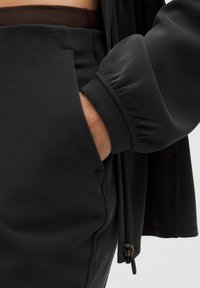 Čierna mikina na zips s nafúknutými rukávmi a predným vreckom, doplnená o zladené čierne nohavice. Hladká textúra látky.