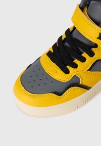 High-top sneaker featuring a combination of yellow and gray leather, black laces, perforated toe box, and a cream-colored rubber sole.