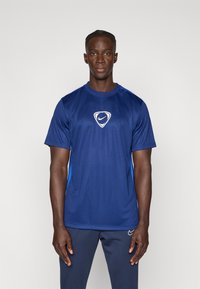 Ναυτικά μπλε αθλητικό μπλουζάκι με λευκό λογότυπο στο κέντρο, με μπλε τόνους στις πλάγιες πλευρές, φτιαγμένο από λεία, ελαφριά ύφανση.