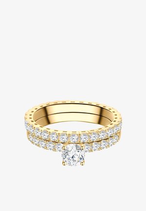 Goldener Ring mit doppelten Reihen kleiner Diamanten und einem größeren runden Diamanten in der Mitte vor weißem Hintergrund.