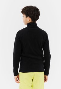 Czarny sweter z golfem, z długimi rękawami, gładka tekstura, dopasowany krój. Noszony z jasnosłonecznymi spodniami, widok z tyłu.