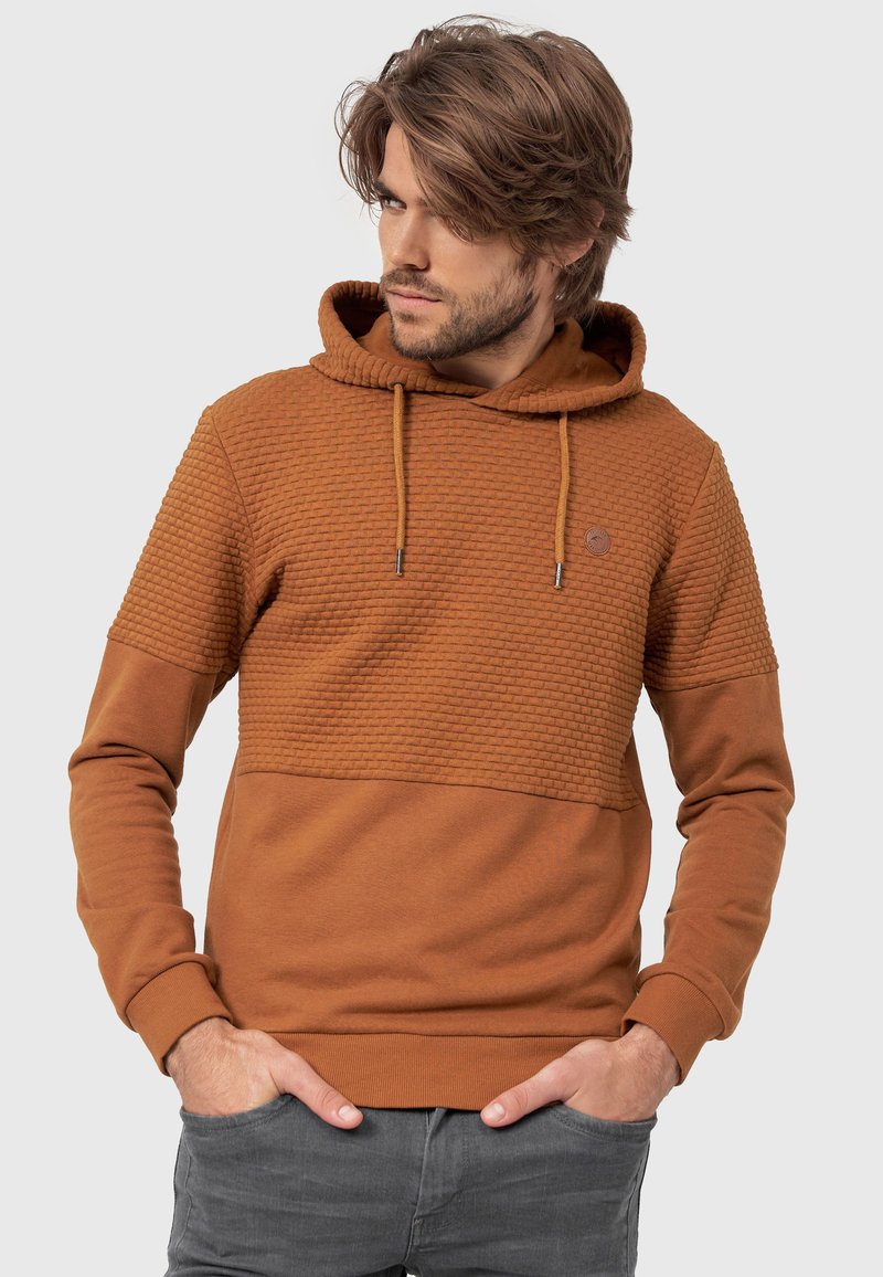 Haut en hoodie marron texturé avec une section inférieure unie, des cordons de serrage et un petit logo sur la poitrine. Le matériau semble doux et décontracté.