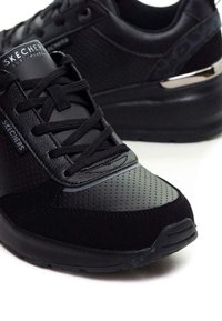 Scarpe da ginnastica nere con una combinazione di pelle liscia e perforata, presentano un accento nero lucido sul tallone e lacci neri piatti.