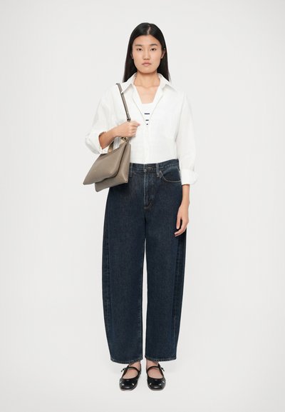 Jeans a vita alta in denim scuro, blusa bianca sopra un top a righe, borsa grigia e scarpe basse nere.