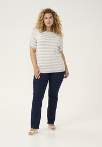 Beige en witte gestreepte gebreide top met korte mouwen, gecombineerd met donkerblauwe denim jeans en witte sandaaltjes met banden. Eenvoudig ontwerp en ontspannen pasvorm.
