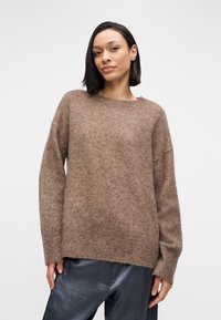 Καφέ πλεκτό πουλόβερ με ελαφρώς χαλαρή εφαρμογή, στρογγυλή λαιμόκοψη και ριμπ μανσέτες. Το ύφασμα φαίνεται μαλακό με υφή.