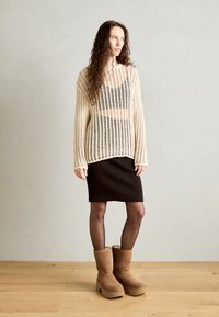 Suéter de malha aberta creme, saia ajustada preta e botas plataforma castanhas até à altura da panturrilha. Material texturizado e corte descontraído com mangas longas.
