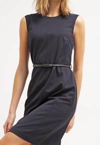 Granatowa sukienka bez rękawów z dopasowaną talią, teksturowanym materiałem, okrągłym dekoltem i cienkim paskiem. Długość do kolan z gładkim wykończeniem.