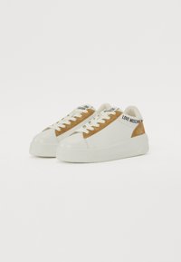 White sneakers with a tan suede panel, round toe, flat rubber sole, and laces. Features "LOVE MOSCHINO" branding on the heel and tongue.