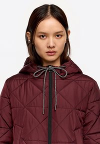 Bordowa pikowana kurtka z kapturem, wyposażona w czarny zamek błyskawiczny, regulowane szare ściągacze oraz teksturę w diamentowy wzór.