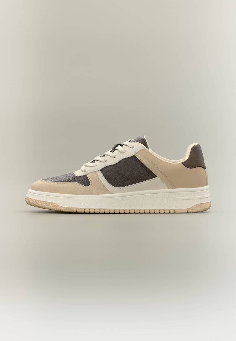 Vue de côté d'une chaussure basse beige, marron et crème avec fermeture à lacets et semelle texturée sur fond neutre.