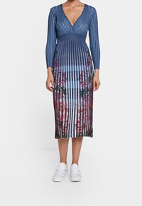 Blårandig klänning med långa ärmar, V-ringning och blommönster vid fållen. Bärs med vita sneakers med färgglada accenter.