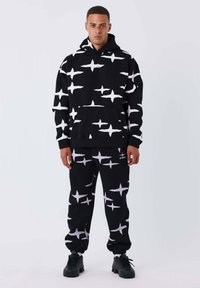 Set di felpa nera con pantaloni tuta, caratterizzato da un motivo astratto bianco. La felpa ha una tasca frontale; l'outfit è realizzato in tessuto morbido con polsini a righe.