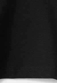 Gros plan d’un tissu noir avec des coutures visibles et une texture tricotée près du bord inférieur.