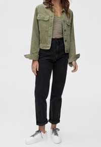 Veste en velours côtelé vert olive avec deux poches poitrine, associée à un jean noir taille haute. Baskets blanches avec des lacets noirs. Haut rayé en-dessous.