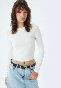 Witte lange mouwen geribbelde crop top met een ronde hals, gecombineerd met een lichtblauwe denim rok en een zwarte riem met een zilveren gesp.