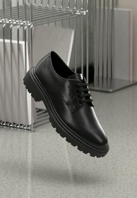 Pantofi din piele neagră cu vârful rotund, talpă groasă din cauciuc și şireturi decorative cu branding embosat pe lateral.