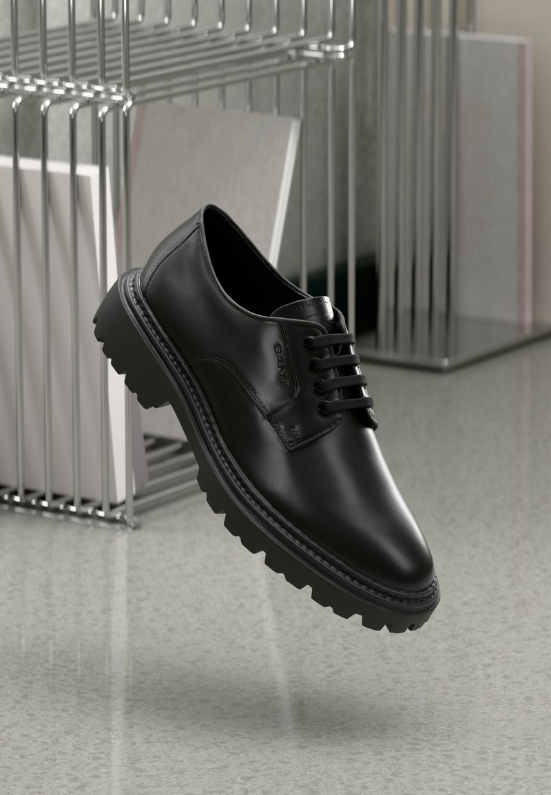 Schwarze Lederschuhe mit runder Spitze, dicker Gummisohle und dekorativen Schnürsenkeln, die ein geprägtes Branding an der Seite aufweisen.