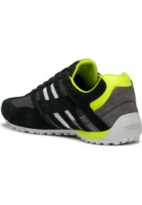 Schwarze Wildleder- und Mesh-Sneaker mit weißen Streifen, gelben Akzenten und einer kontrastierenden grauen Ferse. Verfügt über eine strukturierte weiße Laufsohle.