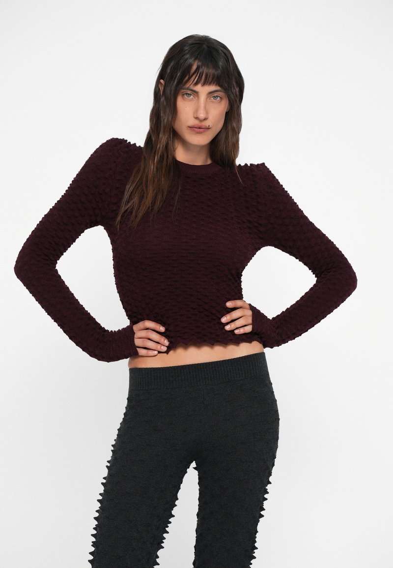 Maglione a maglia testurizzata color bordeaux con maniche lunghe e orlo scallop, abbinato a leggings a vita alta grigio scuro con effetto a coste e dettagli in 3D.