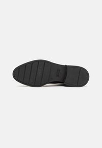 Suela de goma de un zapato, con una superficie texturizada que presenta ranuras horizontales y una punta redondeada, en color negro con el logotipo de la marca visible.