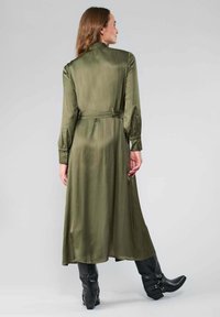 Robe verte olive à manches longues en tissu lisse, avec une taille ceinturée et des poignets boutonnés, dotée d'une jupe longue et fluide.