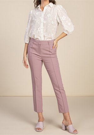 Kvinde iført hvid broderet bluse med pufærmer, støvet rosa skræddersyede ankellange bukser og lyserøde åbne blokhælssandaler.