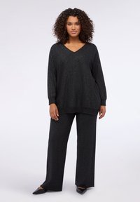 Set lounge nero con scollo a V, maniche lunghe e pantaloni a gamba larga. Il tessuto ha una finitura lucida e testurizzata con un leggero scintillio.