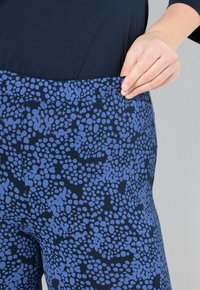 Persona che indossa pantaloni a motivi blu navy e blu chiaro, tirando l'elastico verso l'esterno per mostrare la vestibilità, indossando una maglietta blu scuro.