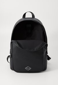 Zaino nero realizzato in materiale sintetico testurizzato. Presenta una forma arrotondata, chiusura con zip e logo frontale. L'interno è foderato con un tessuto liscio.