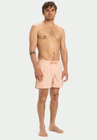 Vaaleanpunaiset uimapuvut, joissa on joustava vyötärö, nyöri ja sivuraidat. Pehmeä kangas, polven ylle ulottuva pituus ja rento istuvuus.