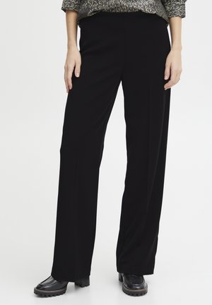 Pantalons larges noirs avec une texture lisse, taille haute et un léger drapé. Associés à des bottes à talons épais noires.