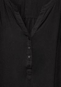 Blouse noire avec un décolleté en V, patte de boutonnage à l'avant comprenant six boutons, et détails froncés au niveau du yoke. Tissu lisse avec une finition mate.