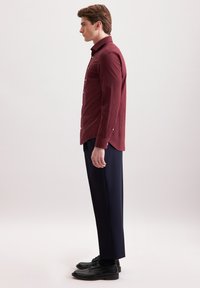 Camicia bordeaux a maniche lunghe con dettagli a bottone abbinata a pantaloni blu navy e scarpe nere. Tessuto morbido, design slim fit.