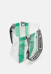 Sac fourre-tout transparent avec des rayures vertes et des sangles de marque noir et blanc, debout sur fond blanc.