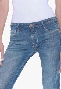 Jeans de denim azul deslavado con cierre de botón, cinco bolsillos y detalles de costura en contraste. Ajuste slim con ligeras marcas de uso.