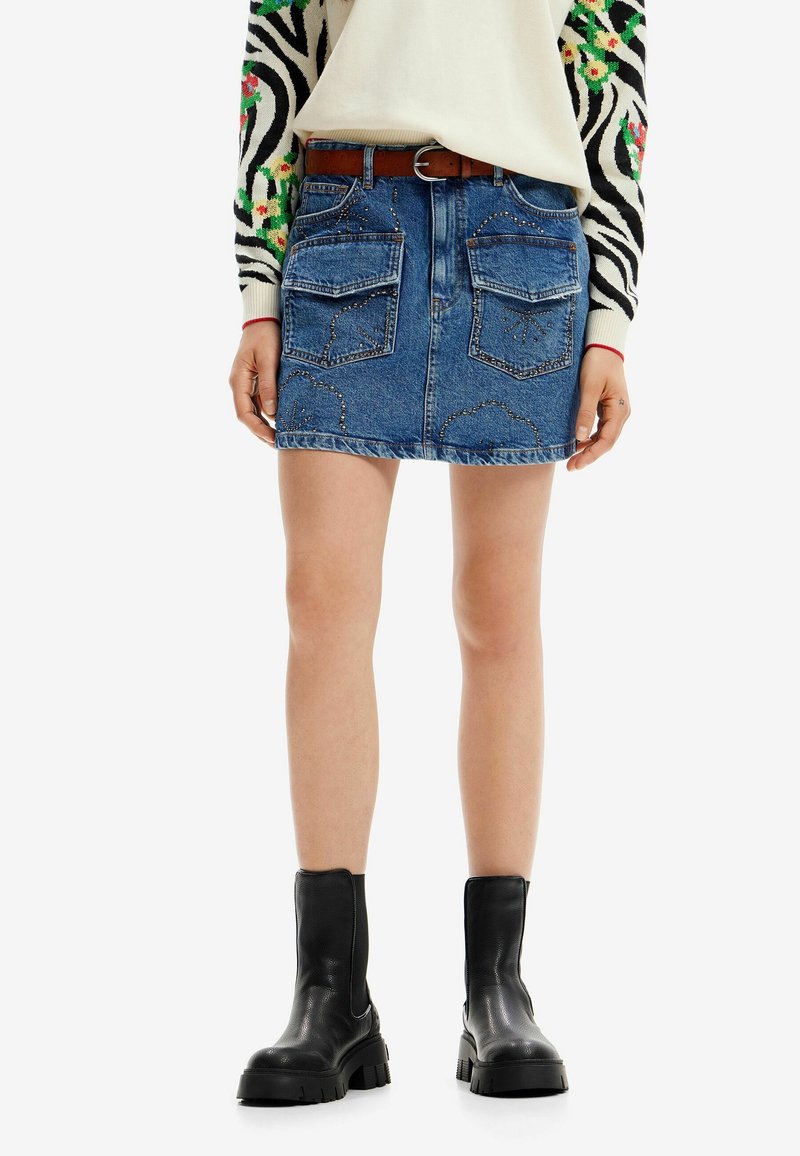 Džínová mini sukně s předními a zadními kapsami, ozdobným šitím a roztrhaným lemem. V kombinaci s černými kotníkovými botami.