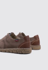Zapatos de ante marrón con detalles perforados, acentos de piel y una suela de goma texturizada con un patrón moteado.