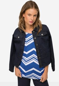 Ciemnoniebieska dżinsowa kurtka z zapięciem na guziki i kieszeniami na piersi, połączona z bluzką w niebiesko-białą kratkę w zygzaki. Gładka faktura.