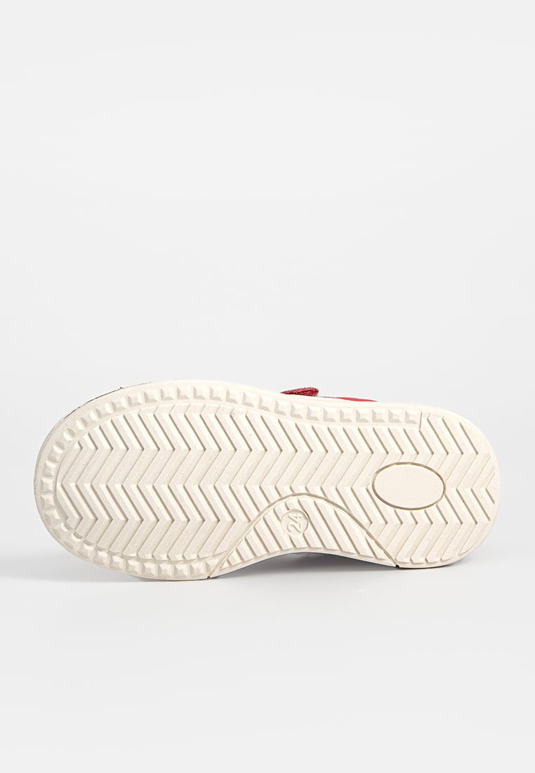 Sohle eines weißen Sneakers mit einem Fischgrätprofil und einem kleinen ovalen Detail in der Nähe der Ferse, vor einem schlichten Hintergrund.
