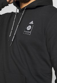 Svart huvtröja med framficka, ett vävt märke med den tyska fotbolls emblem och märkta dragsnören med "adidas" text.