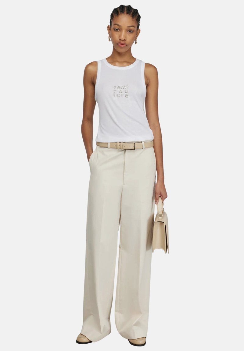 Top bianco senza maniche con testo grafico, pantaloni ampi crema, cintura beige, piccola borsa beige e scarpe color sabbia chiare. Texture lisce.