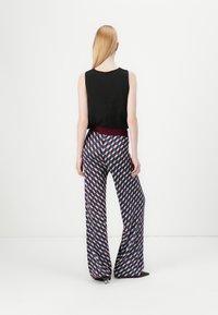 Top nero senza maniche abbinato a pantaloni a gamba larga con un motivo geometrico in rosso, blu e crema. Tessuto morbido, vita aderente.