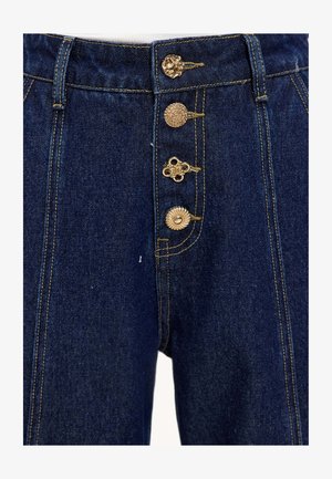Hochgeschnittene blaue Jeanshose mit goldenen Dekoknöpfen, Kontrastnähten und einem leicht strukturierten Stoff.