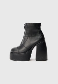 Bota de cano curto em pele preta com salto bloco alto, apresentando padrões de costura, fecho de correr e design de biqueira arredondada.