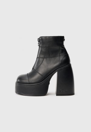 Bota de cano curto em pele preta com salto bloco alto, apresentando padrões de costura, fecho de correr e design de biqueira arredondada.